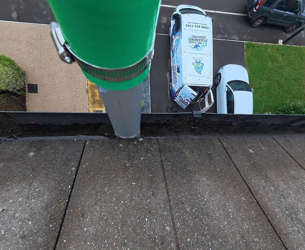 Gutter clearing pole working along a roof edge, with our van on the drive below
