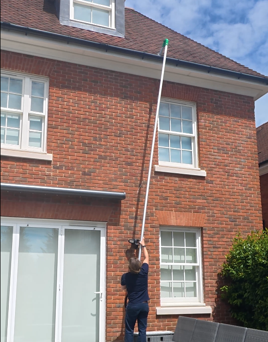 Clearing gutters at a brick house using a long pole from the ground